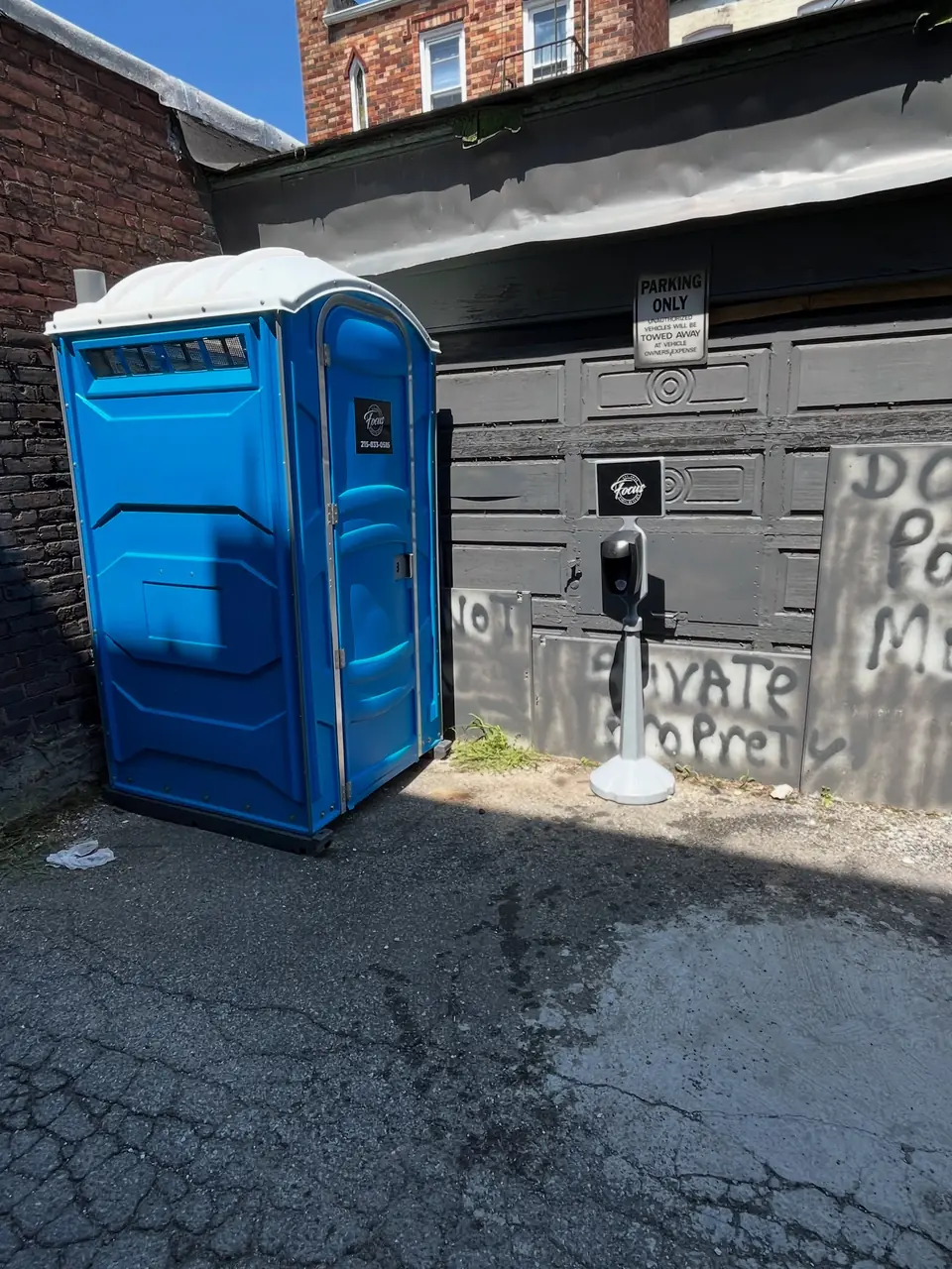 Blue porta potty set in a paved alley behind a brick building
