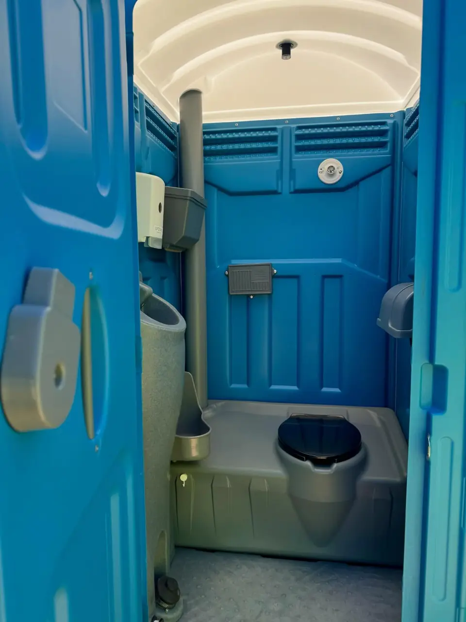 Inside a blue standard porta potty: toilet seat, urinal, vent pipe and paper holder