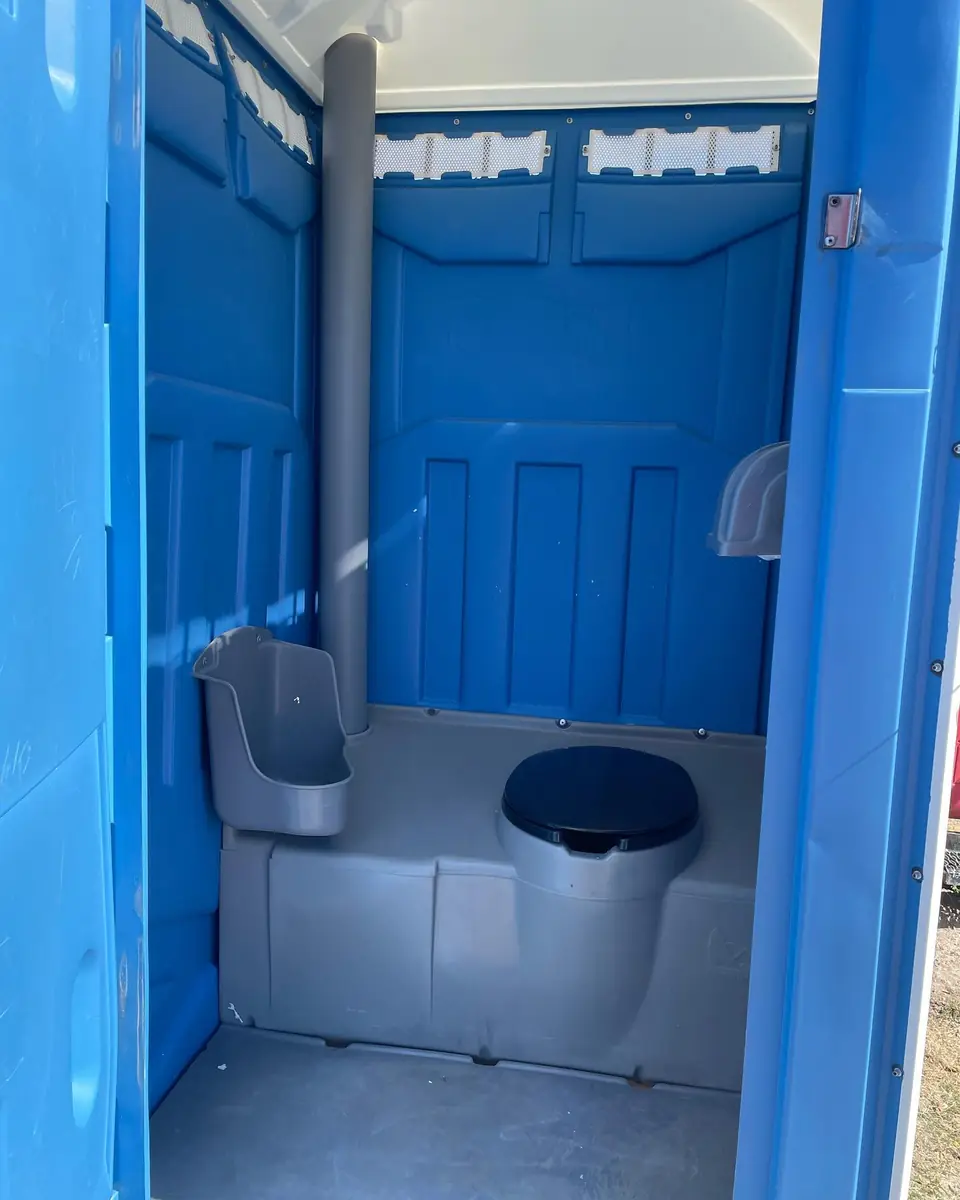 Interior of a blue porta potty showing the seat, urinal and roof vent stack