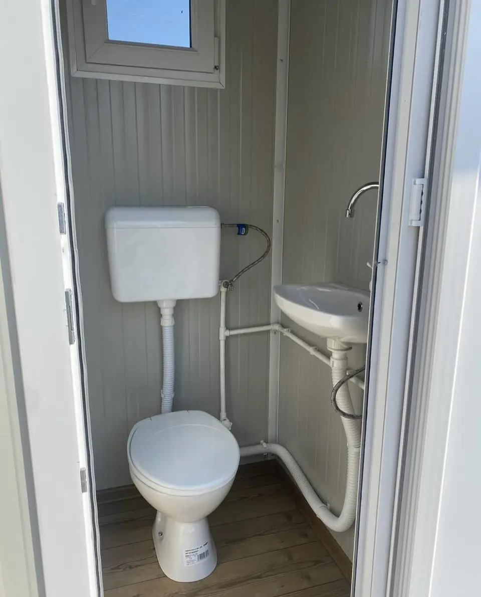 Flushing toilet and small corner sink inside a white portable restroom cabin