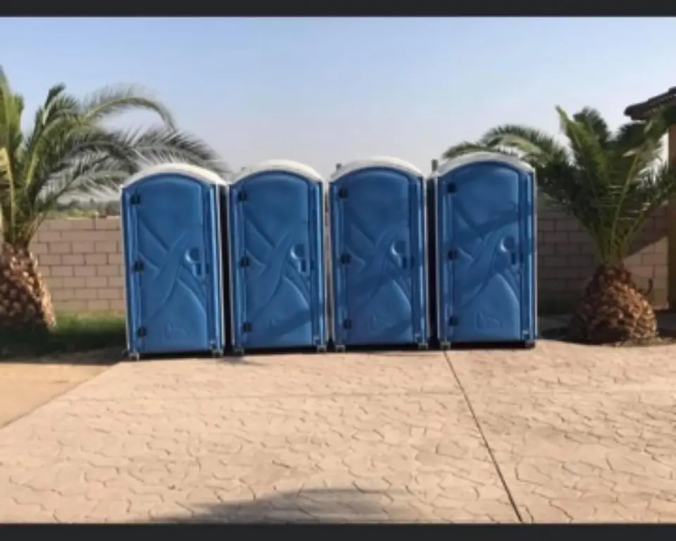 Four blue porta potties in a row on a stamped concrete patio between palm trees