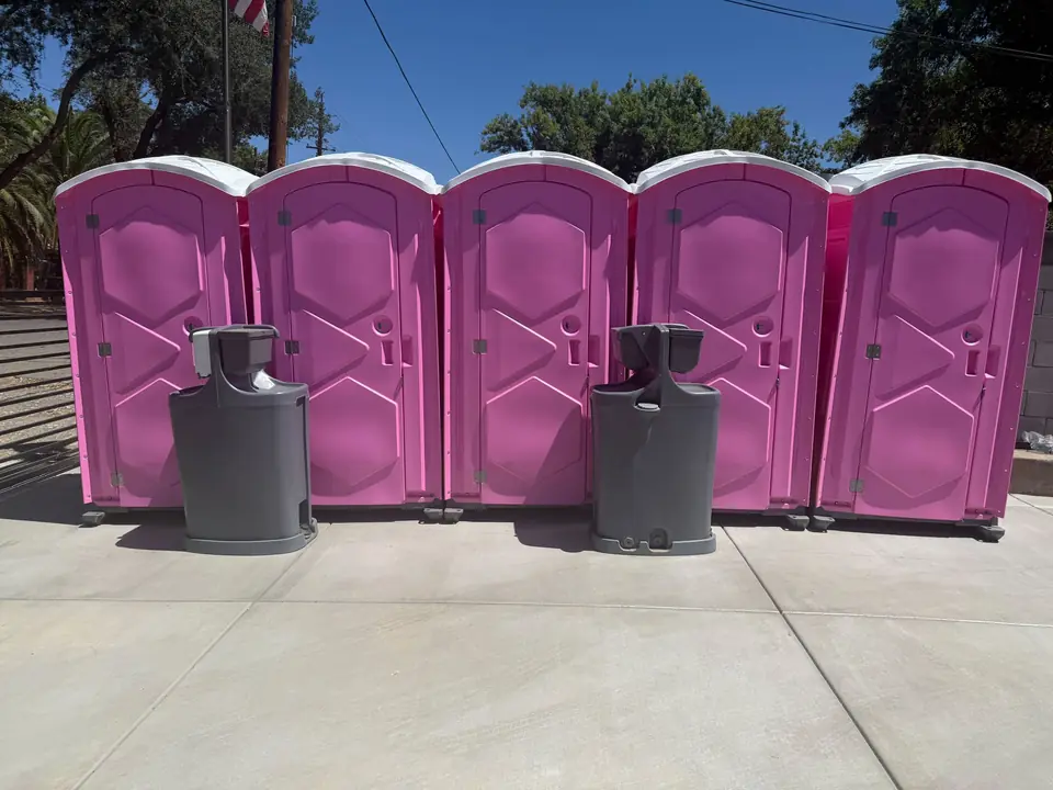 Row of five pink portable toilets with two freestanding hand-wash stations on a concrete pad