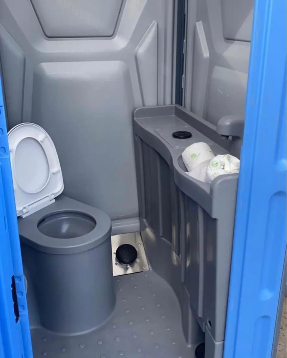 Gray porta potty interior with seat and toilet paper dispenser stocked with rolls
