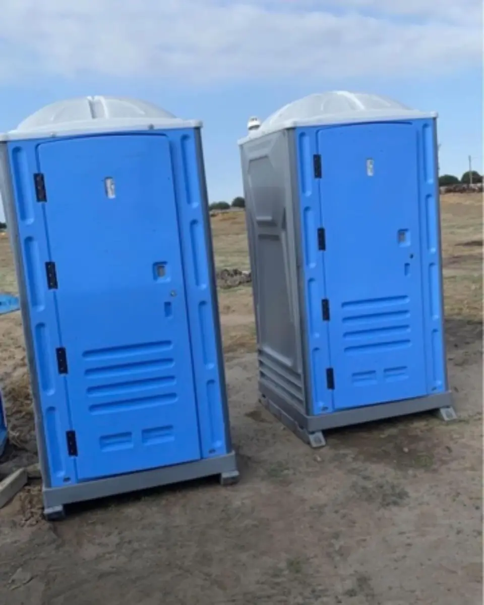 Two blue standard porta potties on bare dirt at a construction lot